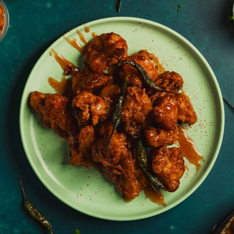 Chicken tikka bites glazed in chili, on a green plate